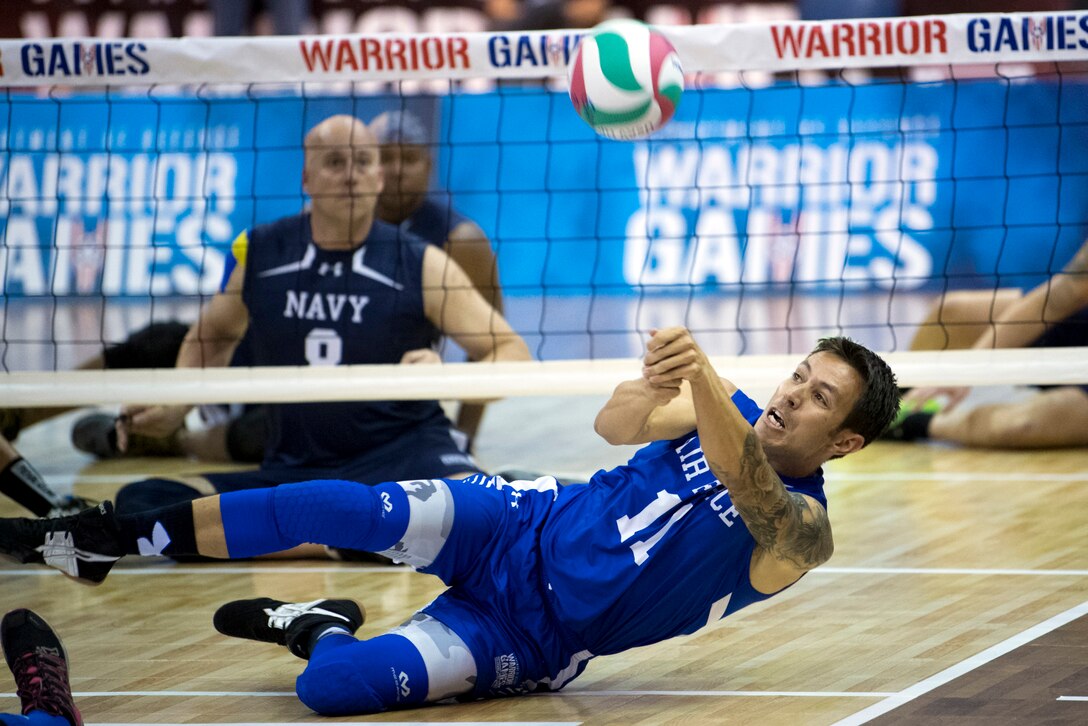 An sitting airman leans toward the gym floor while setting a volleyball.