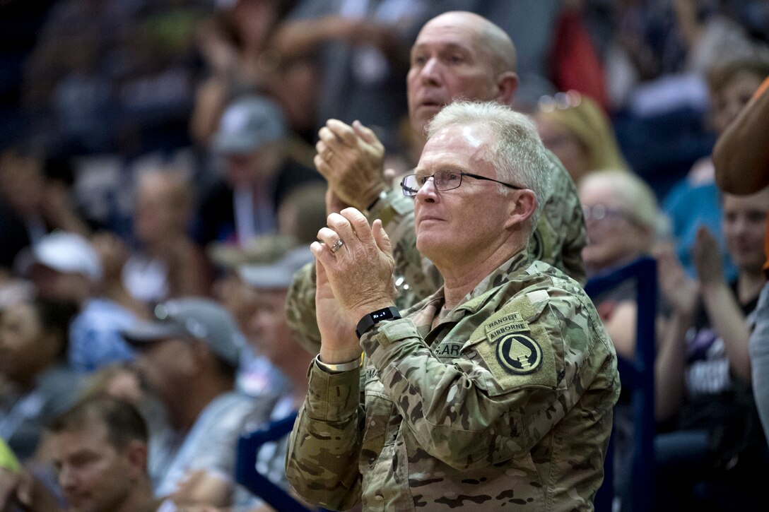 Army Raymond A. Thomas III stands and applauds in a crowd.