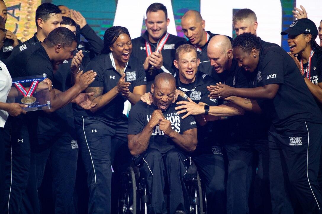 Teammates cheer for an athlete seated in a wheelchair while gathered around him.