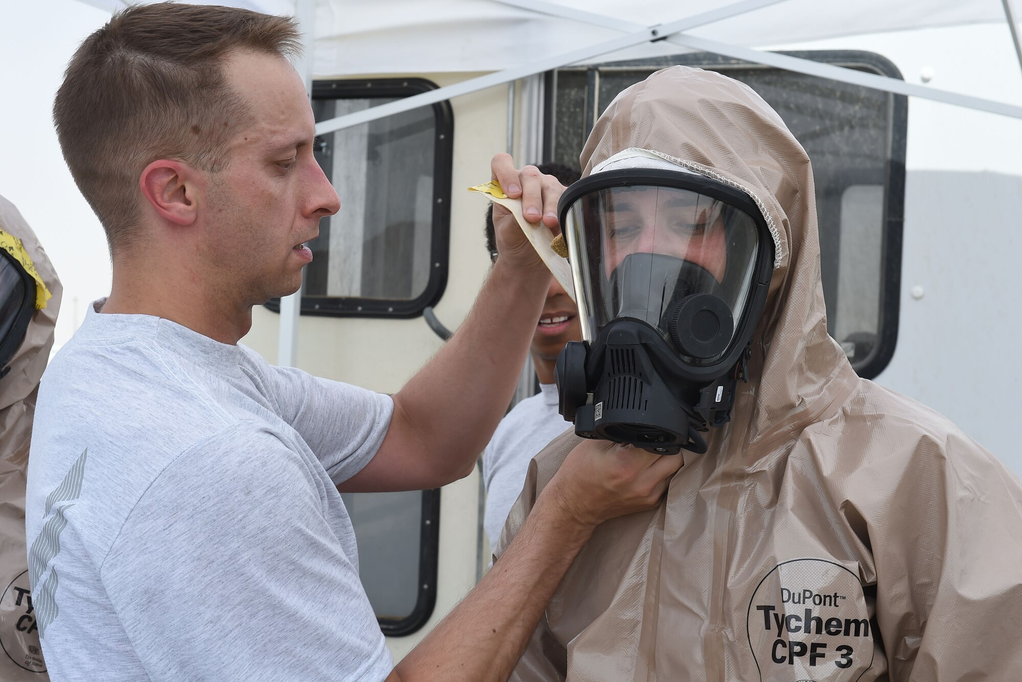 Airman helps another Airman by putting tape around the seal of his face mask