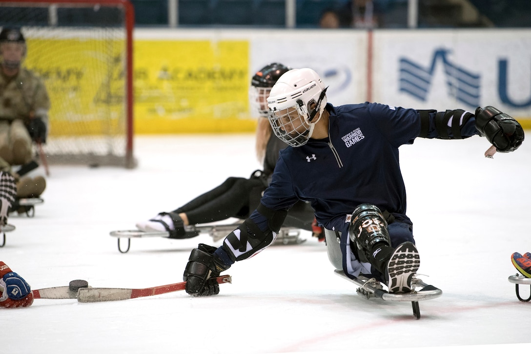 A sailor battles for the puck during an exhibition sled hockey game.