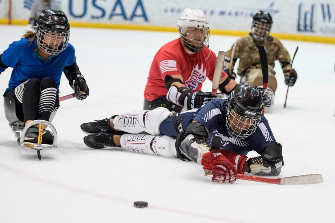 Sailors battle for the puck in an exhibition sled hockey game.