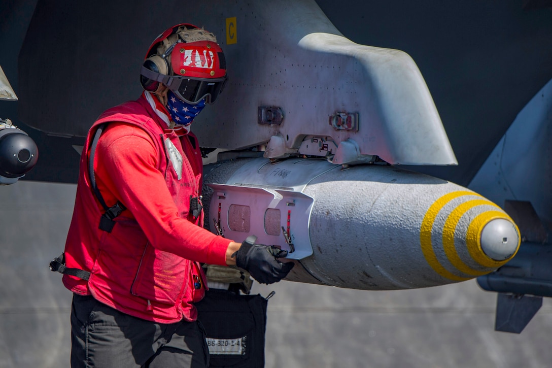A sailor looks at ordnance attached to an aircraft.