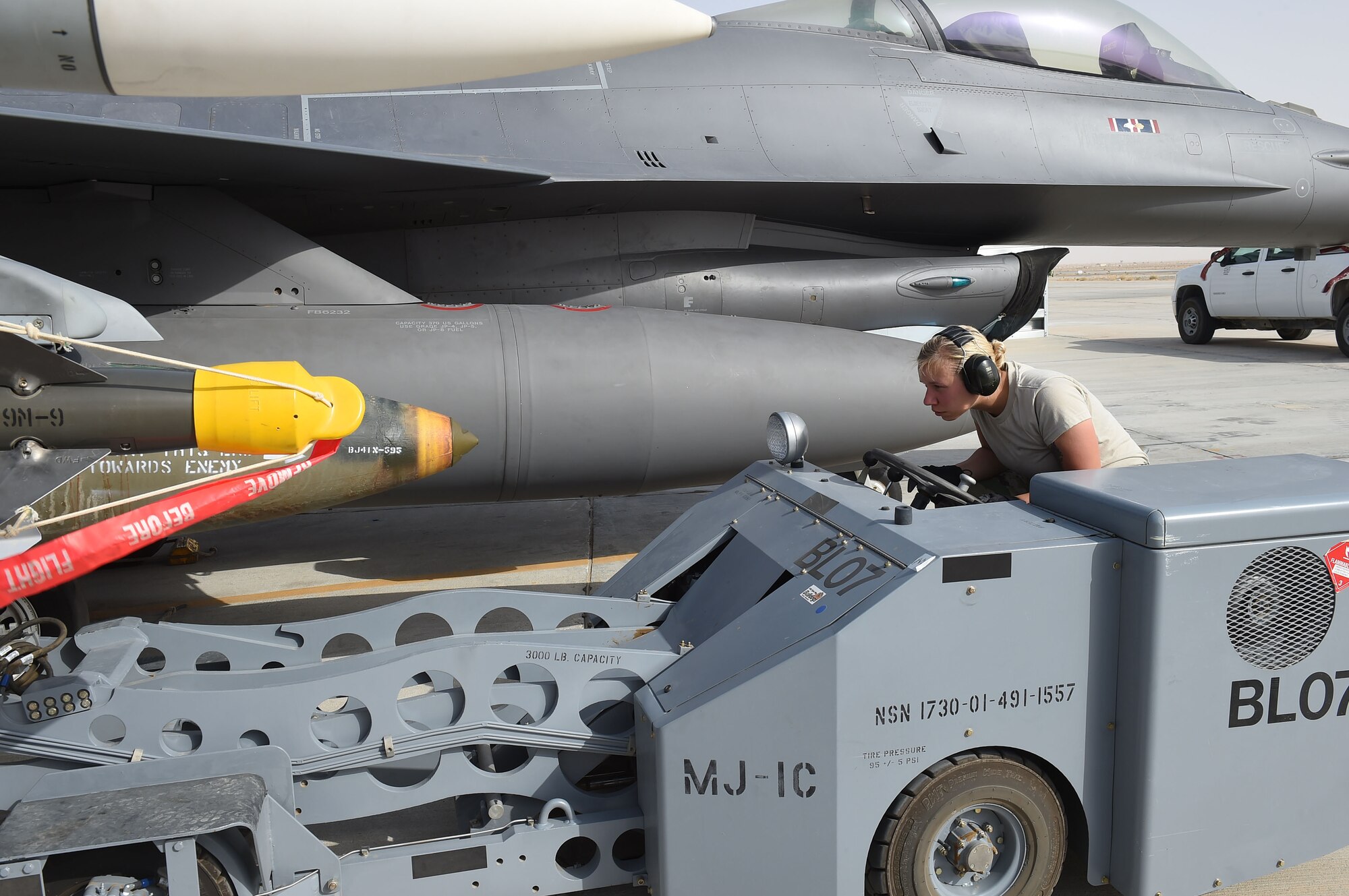 female airman attaches bomb to jet with small vehicle