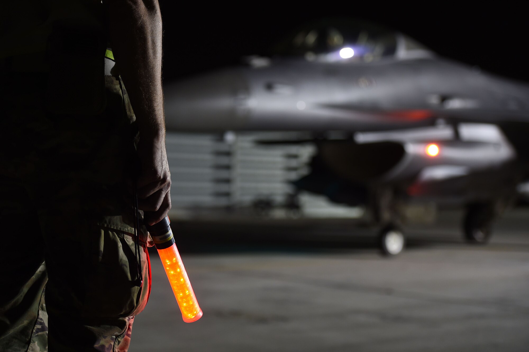 crew chief hold light in front of jet at night time.