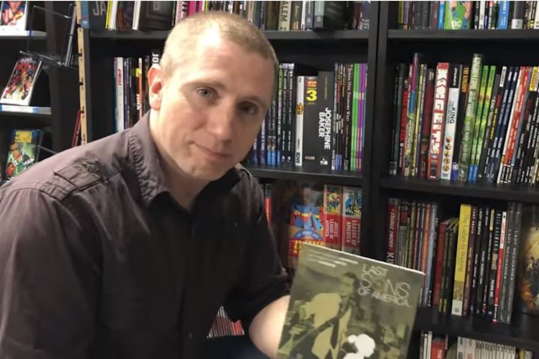 A man poses for a photo holding a book.