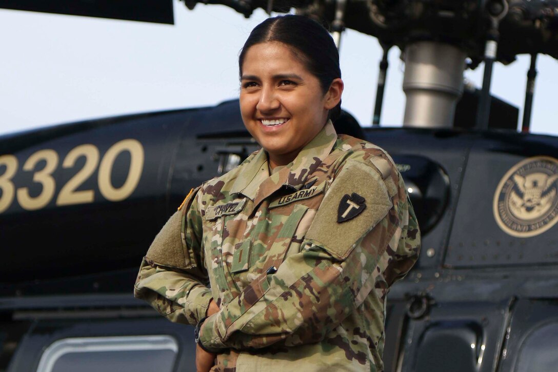 A female soldier poses in front of a helicopter.