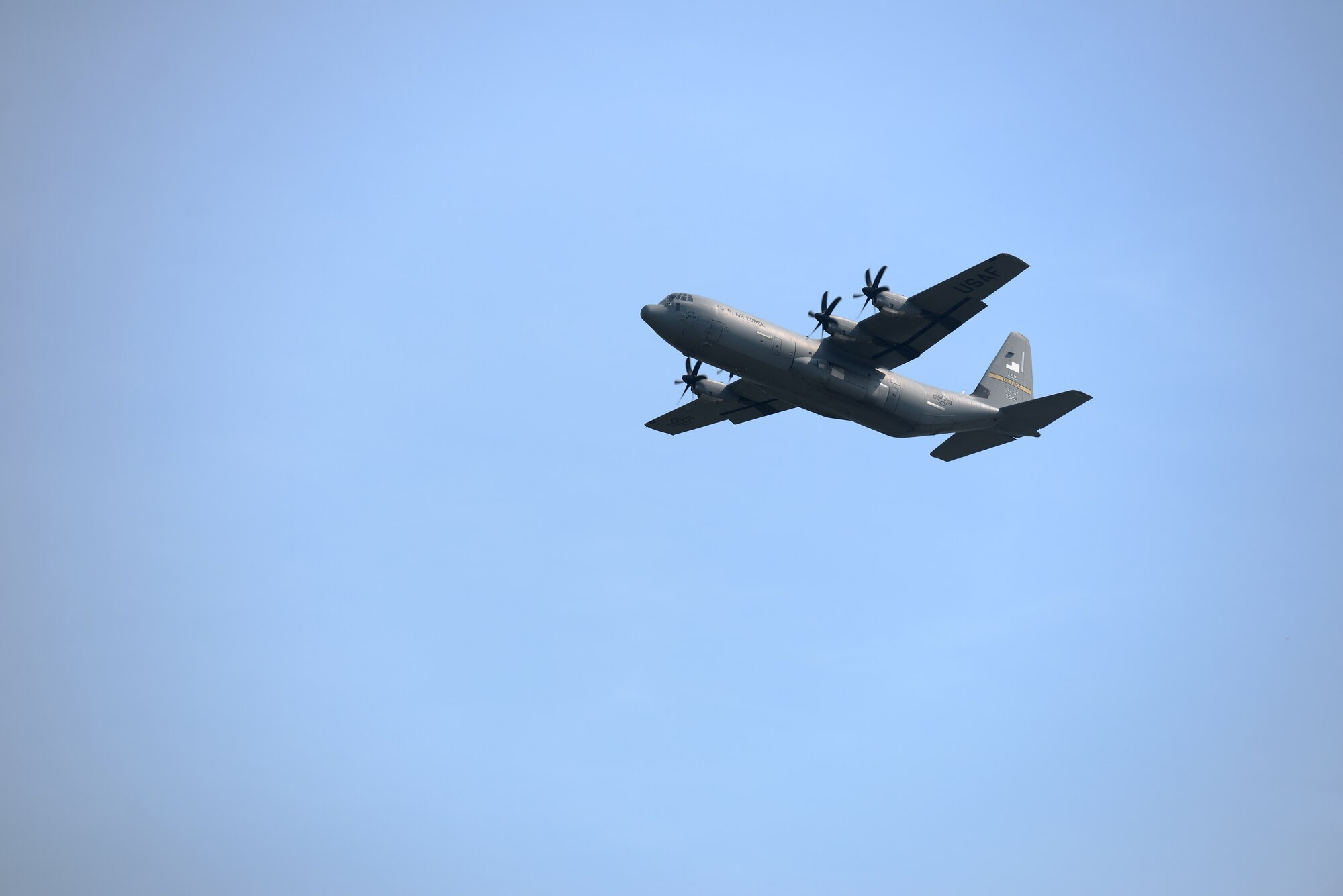 A C-130J aircraft flies in the sky going from right to left just after takeoff