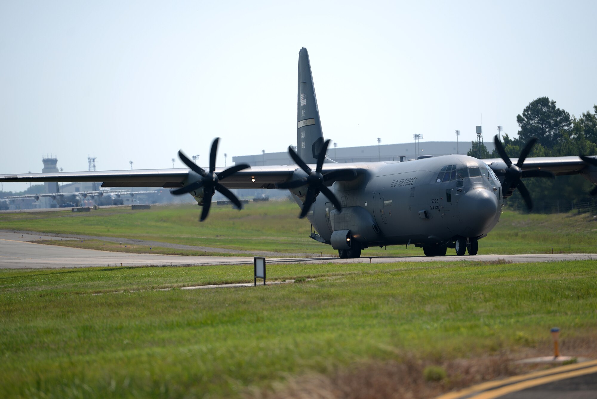 A C-130J Aircraft is taxing from left to right with the flight line behind it.