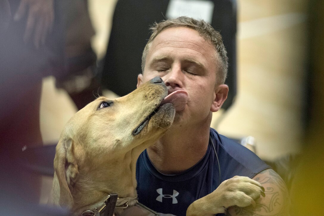 A sailor’s service dog licks his face after an indoor rowing competition.