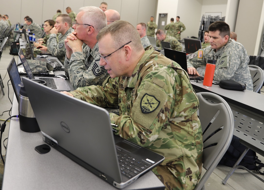 Soldiers and airmen work at laptop computers.