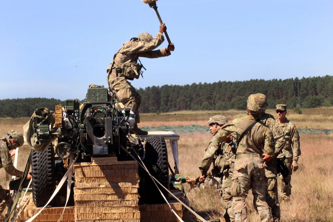 Soldiers remove packaging from an airdropped M119 105 mm howitzer.