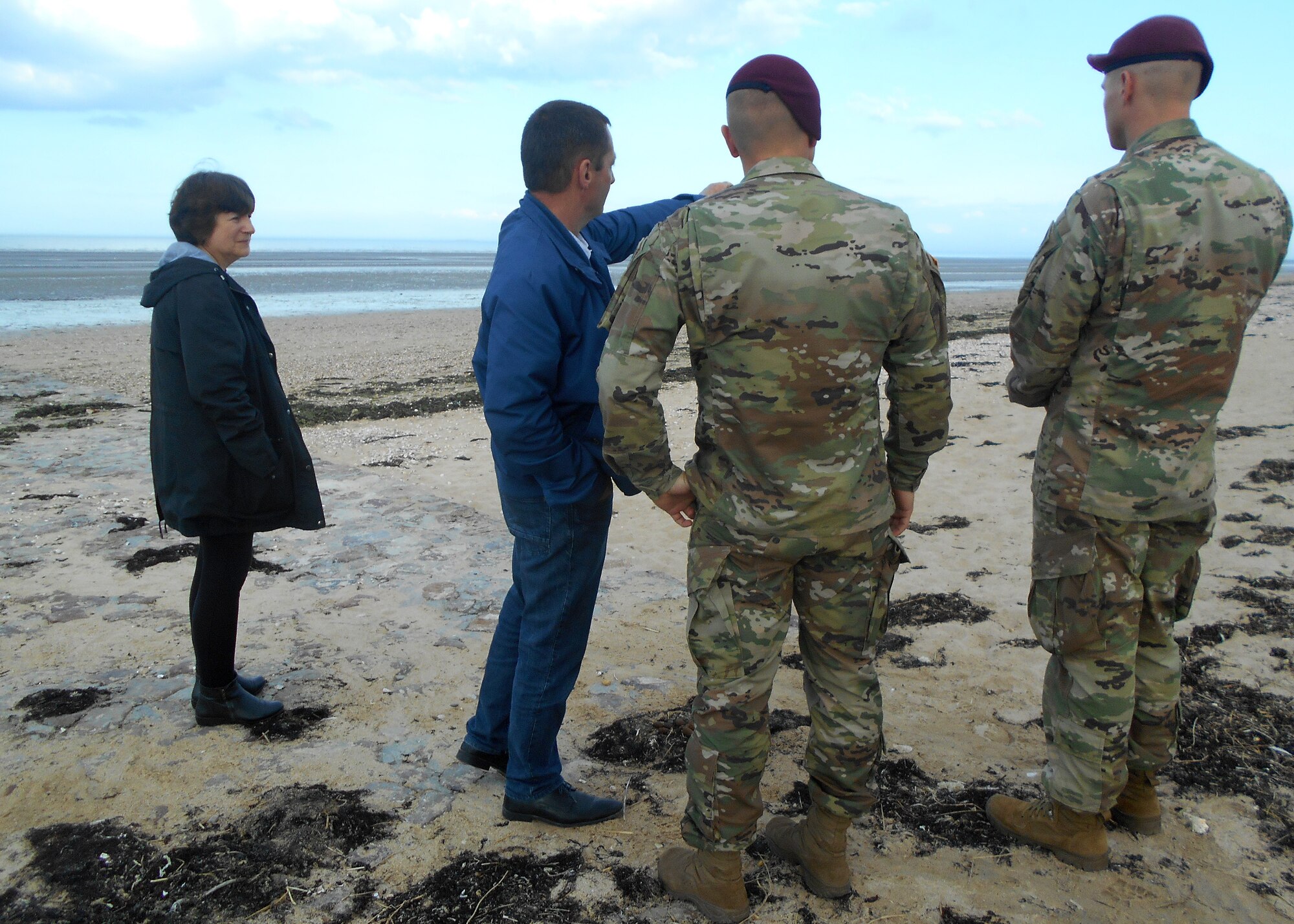 Service member speak to a local on a beach in Normandy, France.