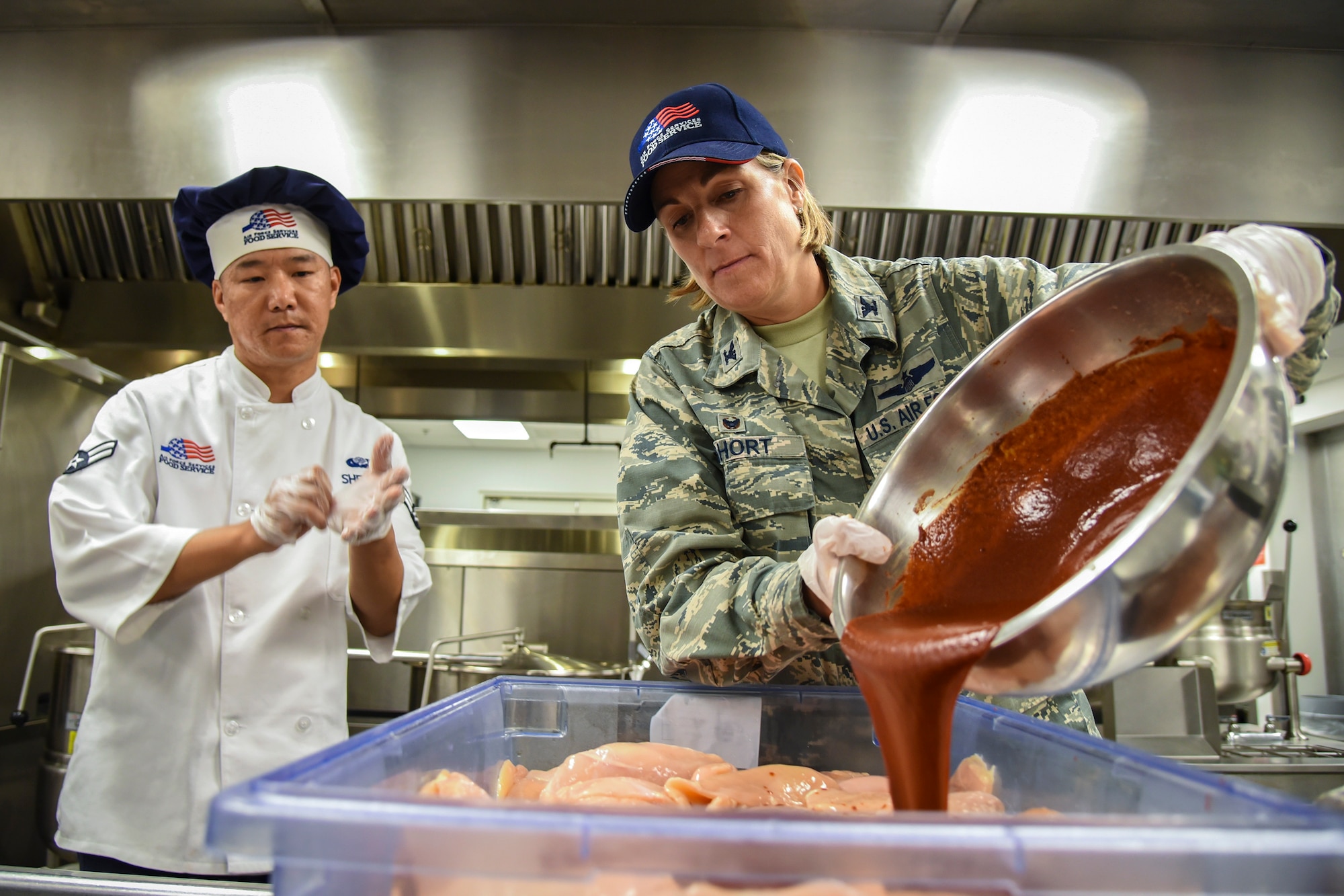 Col. Jennifer Short, right, 23d Wing (WG) commander, pours sauce onto chicken during an immersion tour, June 11, 2018, at Moody Air Force Base, Ga. Short and Chief Master Sgt James Allen, 23d WG command chief  toured the Georgia Pines Dining Facility and the Information Learning Center to gain a better understanding of their overall mission, capabilities and comprehensive duties. (U.S. Air Force photo by Airman 1st Class Eugene Oliver)