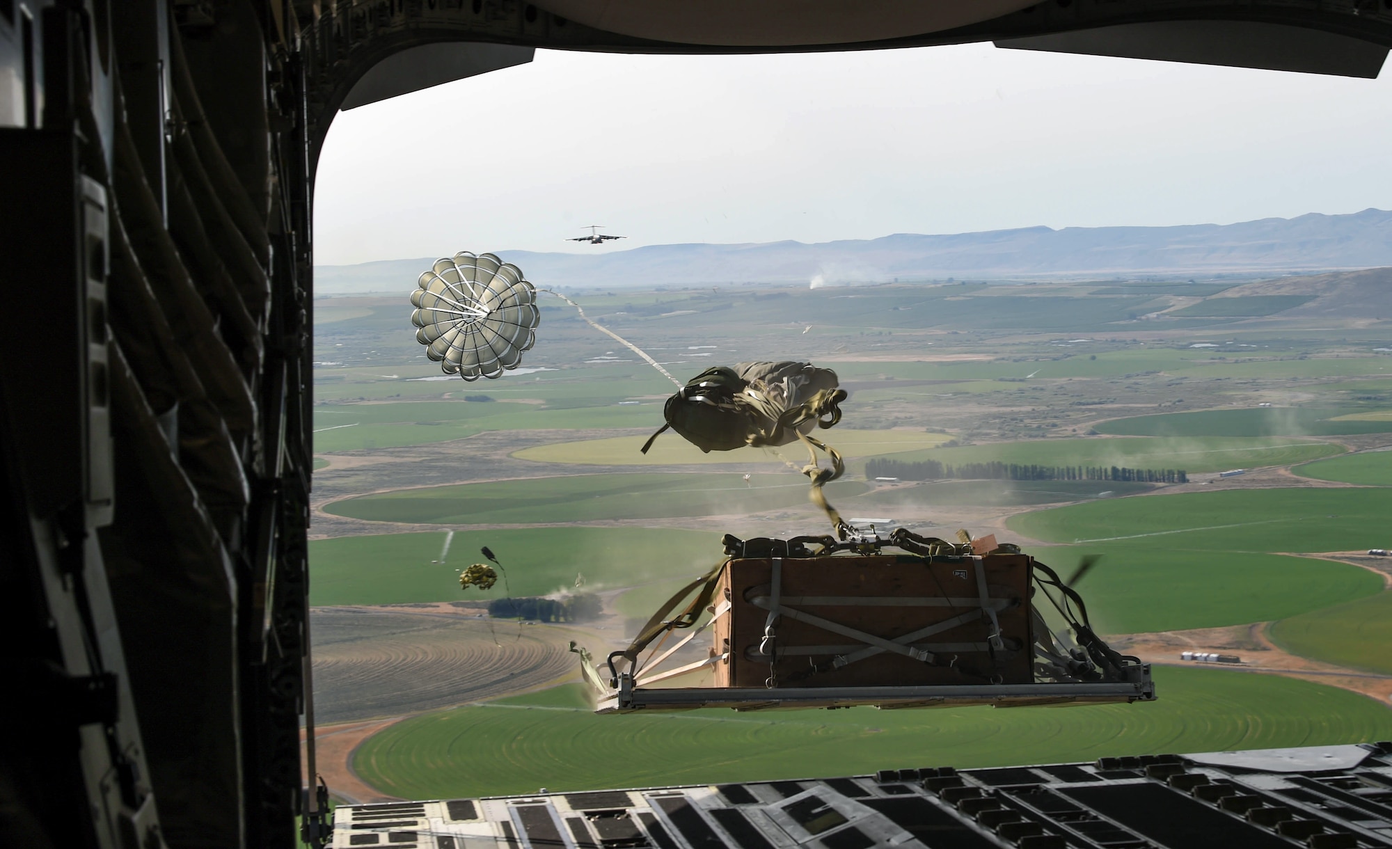 A container delivery system bundle drops out of a C-17 Globemaster III during Exercise Rainier War at the Rainier Drop Zone near Moses Lake, Wash., June 6, 2018. Eighteen C-17s and three KC-135 Stratotankers from McChord Field, other Air Mobility Command bases and Australia participated in Rainier War. (U.S. Air Force photo by Senior Airman Tryphena Mayhugh)