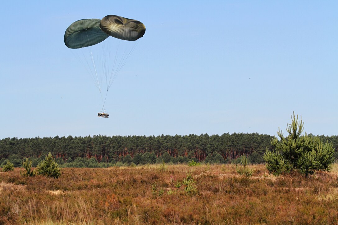 A High Mobility Multipurpose Wheeled Vehicle slowly descends to the ground via parachutes.