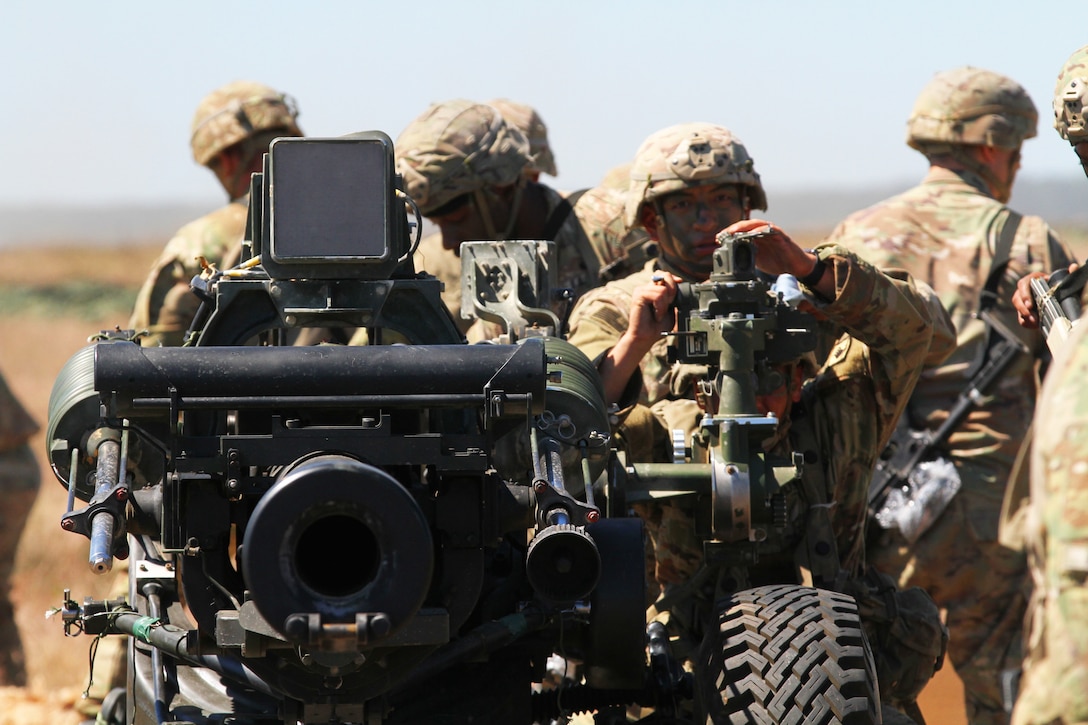 Soldiers make adjustments to an M119 105 mm howitzer.