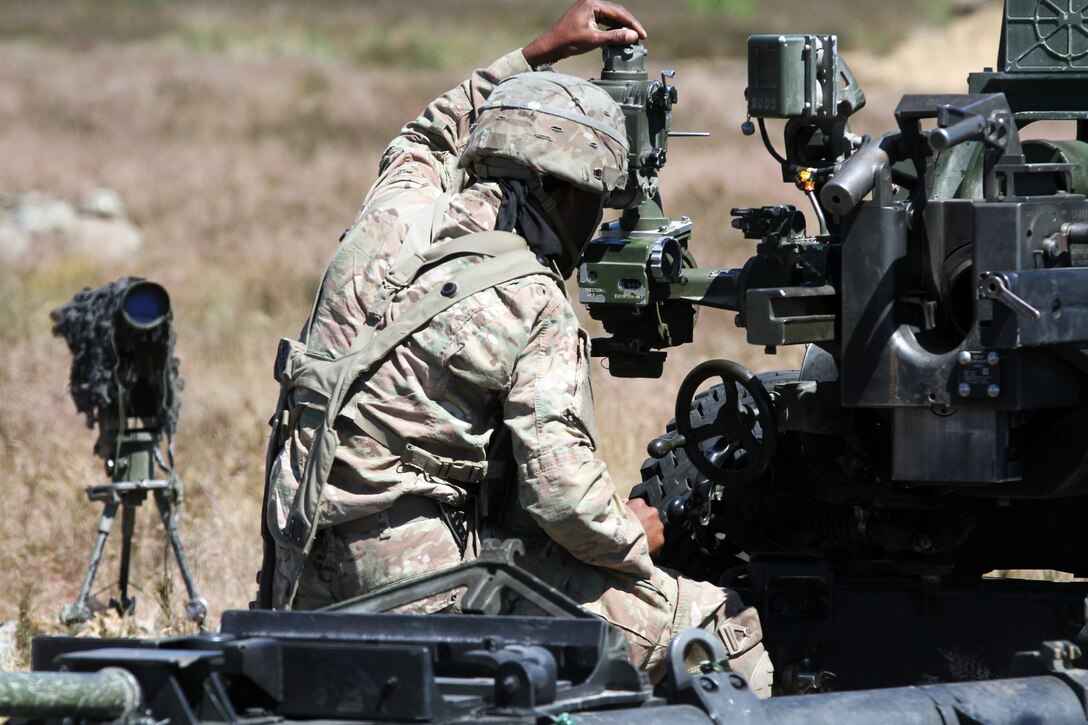 A soldier makes adjustments to a M119 105 mm howitzer.