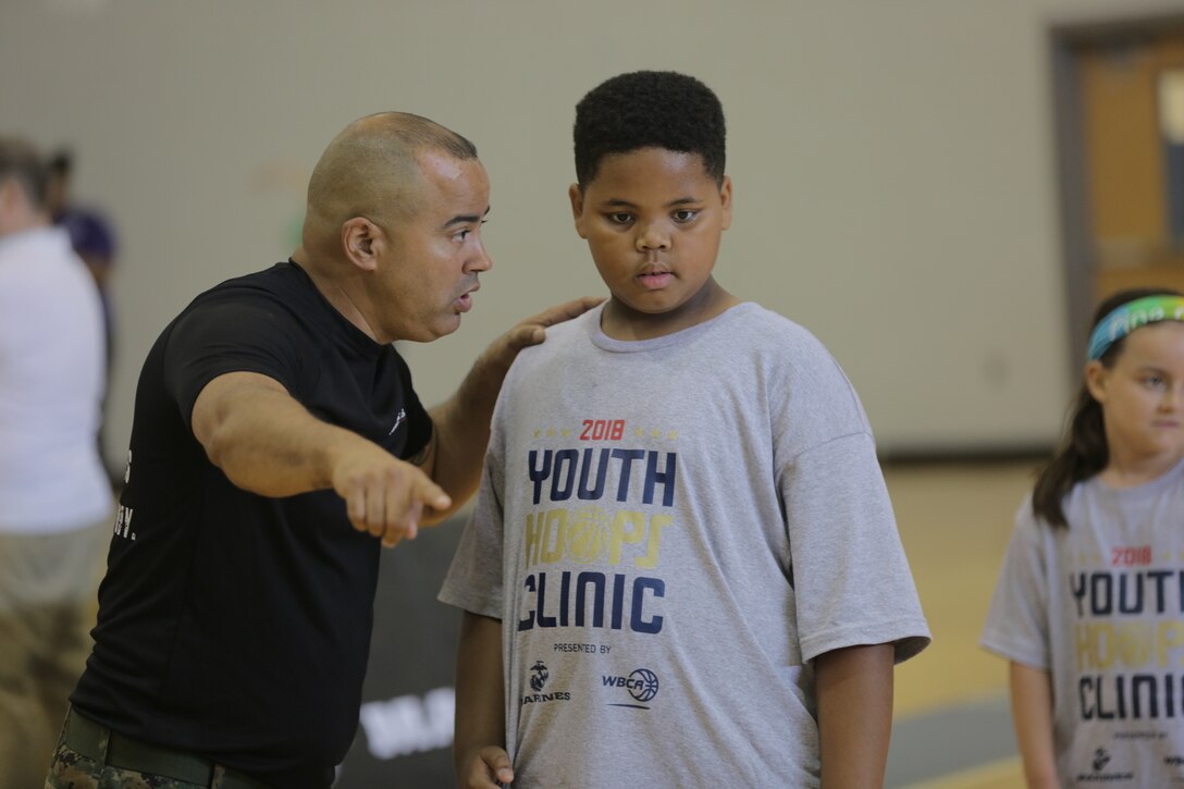 Master Gunnery Sgt. Abiud Montes gives instruction to a young basketball player at the WBCA Hoops Youth Clinic in Dallas, Texas, June 9, 2018. The Marine Corps has partnered with WBCA since 2013 with the goal of increasing awareness and positive perception of the Marine Corps with influencers like coaches and leaders. In 2017, the Marine Corps Recruiting Command created a city partnership program, which focuses on building enduring relationships in six key cities, including Dallas. The youth clinic is an outgrowth of both initiatives. (U.S. Marine Corps photo by Lance Cpl. Haley Gawronski)