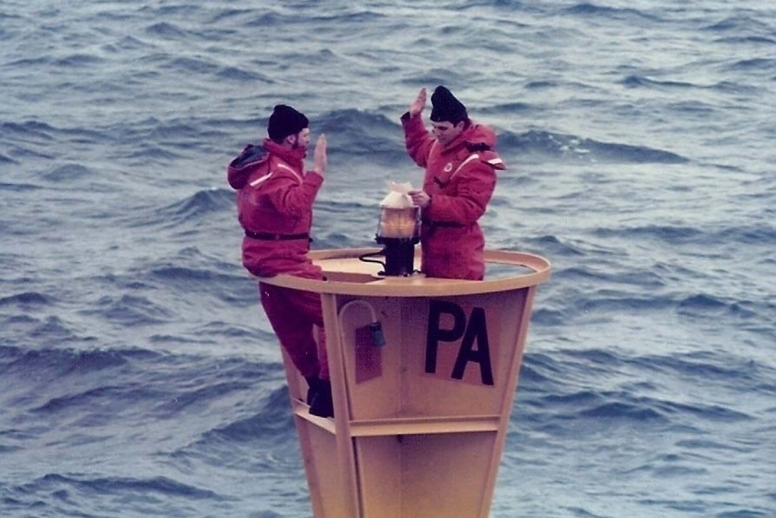 A Coast Guard petty officer reenlists standing on a buoy surrounded by water.