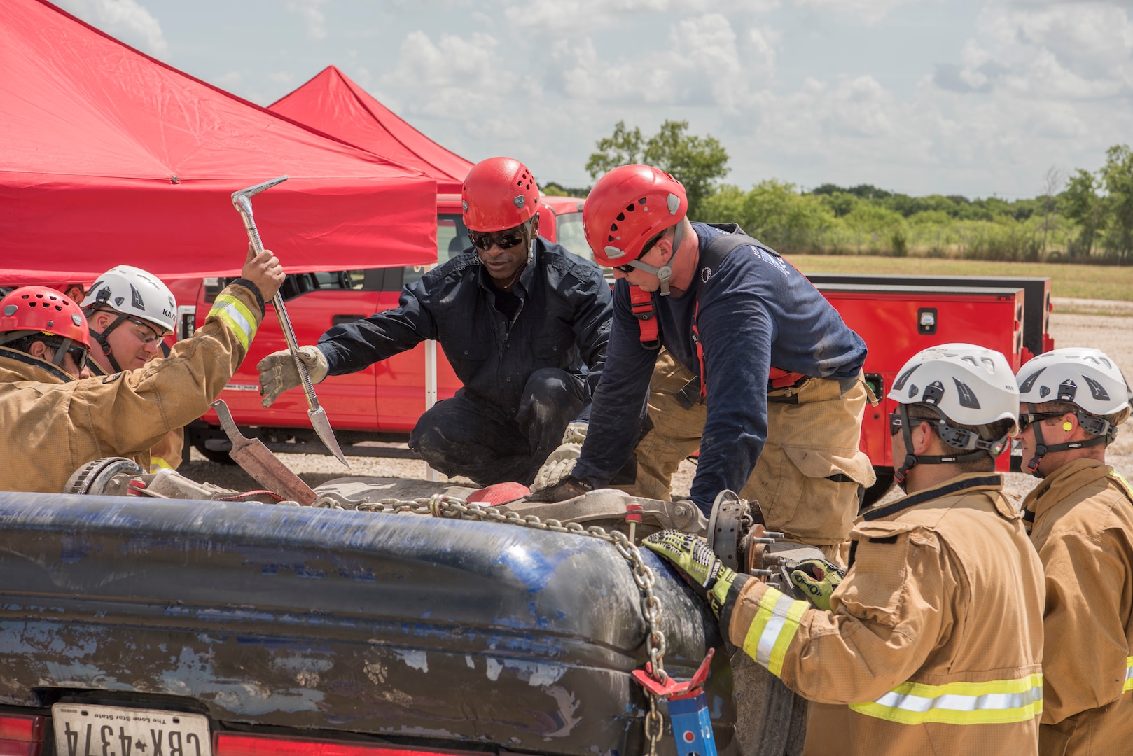902nd Civil Engineer Squadron firefighters work together during a vehicle extrication exercise June 8, 2018, at Camp Talon, Joint Base San Antonio-Randolph. These men used teamwork to remove a full fuel tank from the car to prevent hazards during the simulation.  (U.S. Air Force photo by: Airman Shelby Pruitt.)