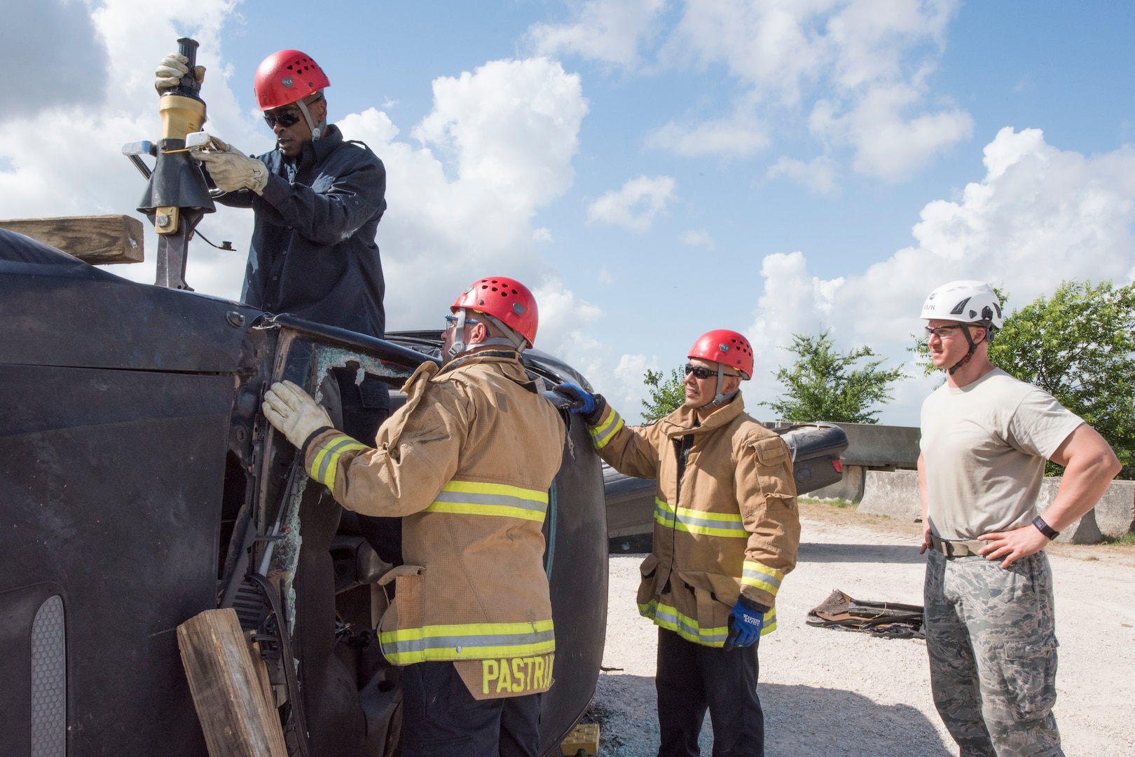 902nd Civil Engineer Squadron firefighters observe a simulated vehicle extrication rescue June 8, 2018 at Camp Talon, Joint Base San Antonio-Randolph. In this scenario, firefighters use a smaller form of the Jaws of Life to push the dashboard off the victim. (U.S. Air Force photo by: Airman Shelby Pruitt.)