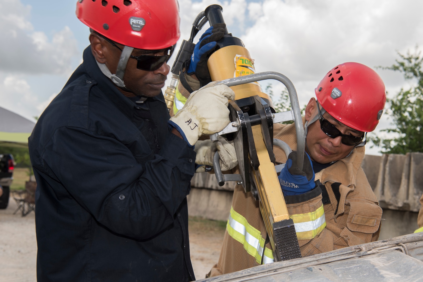 Jesus Rico and Esteban Perez, 902nd Civil Engineer Squadron firefighters, train using the Jaws of Life June 8, 2018 at Camp Talon, Joint Base San Antonio-Randolph. These men use the Jaws of Life to pry the lodged door open and simulate a vehicle extrication rescue. (U.S. Air Force photo by: Airman Shelby Pruitt.)