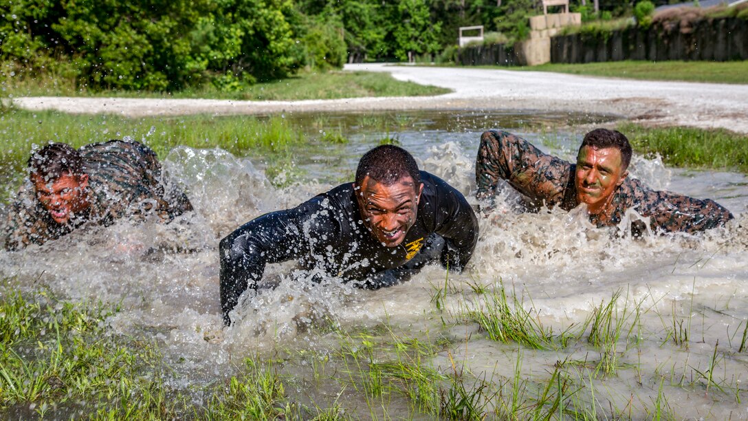 Three Marines splash as they move through a puddle.