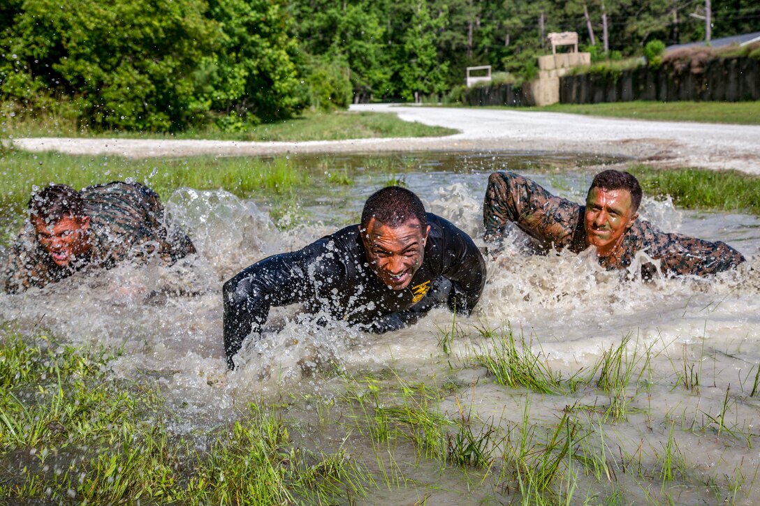 Three Marines splash as they move through a puddle.