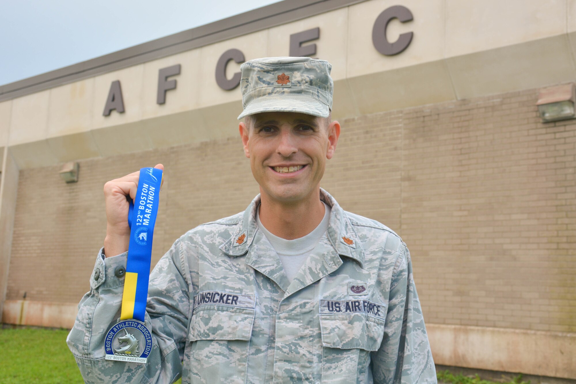 Man wearing Air Force uniform stands and smiles at center holding Boston Marathon completion medal.
