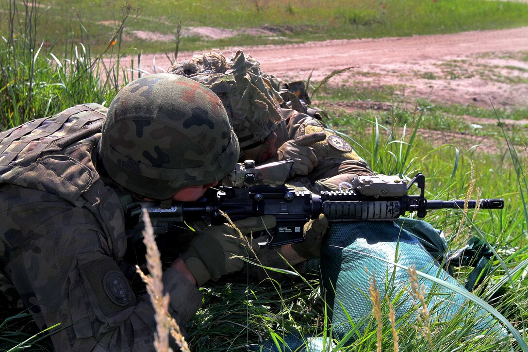 A U.S. soldier instructs a Polish soldier on rifle sight alignment and range estimation.