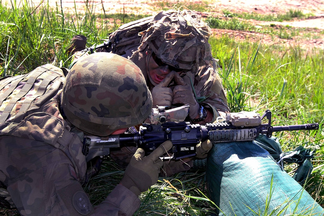 A U.S. soldier uses his hands to demonstrate proper rifle sight alignment to a Polish soldier.