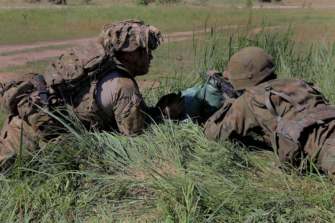 A U.S. soldier instructs a Polish army soldier on rifle sight alignment.