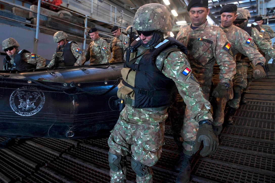 Romanian troops carry a combat rubber raiding craft into the well deck.