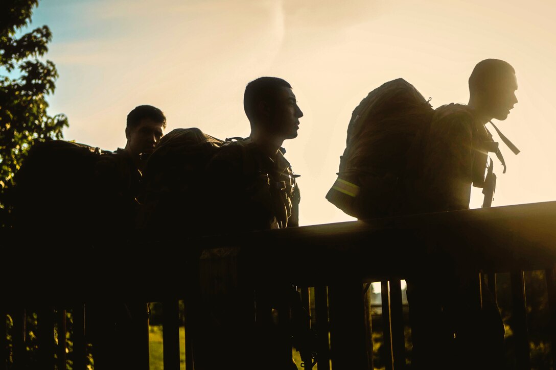 Three Marines wearing packs are silhouetted by the sun.