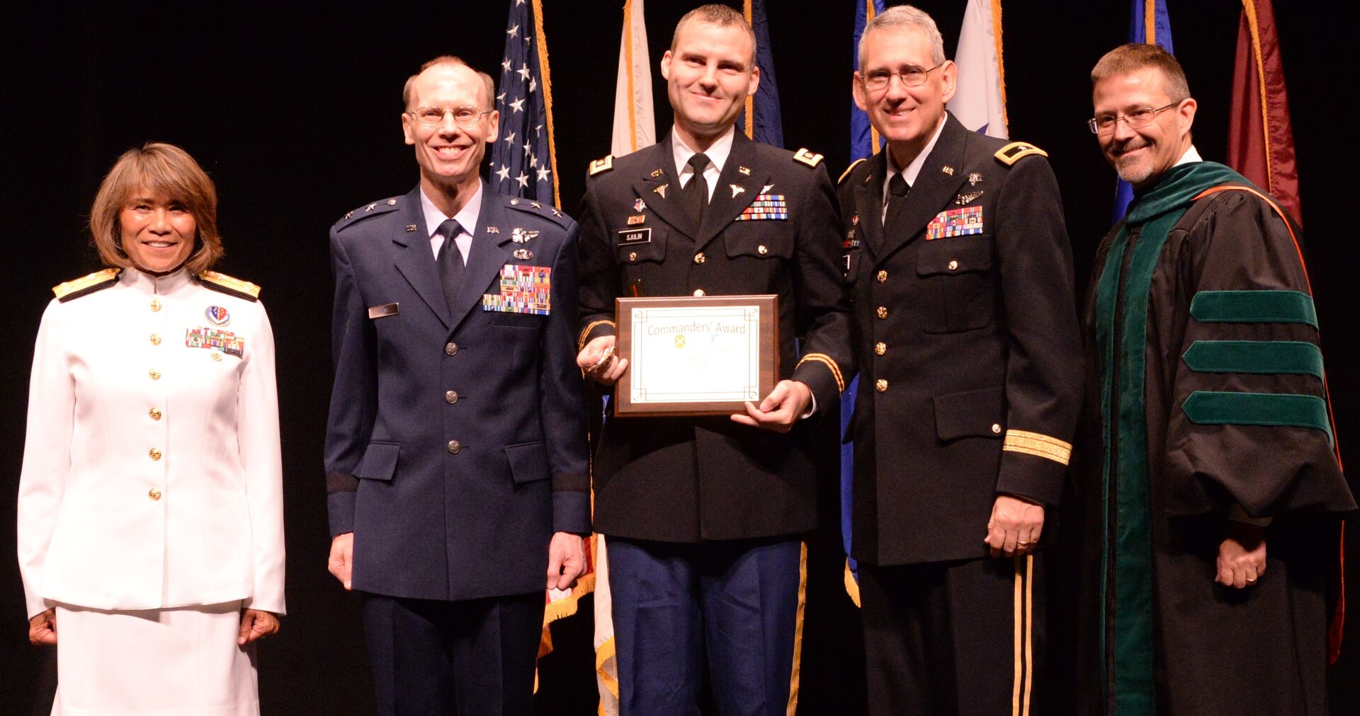 Army Maj. Tyson Sjulin, pulmonary/critical care fellow, receives the Commander’s Award for Fellow Clinical Research during the San Antonio Uniformed Services Health Education Consortium graduation ceremony held June 7 at the Lila Cockrell Theatre in downtown San Antonio. Also pictured are (from left) Vice Adm. Raquel Bono, director of the Defense Health Agency; Air Force Maj. Gen. Bart O. Iddins, 59th Medical Wing commander; Army Brig. Gen. George Appenzeller, Brooke Army Medical Center commander; and Dr. Woodson Scott Jones, dean of SAUSHEC