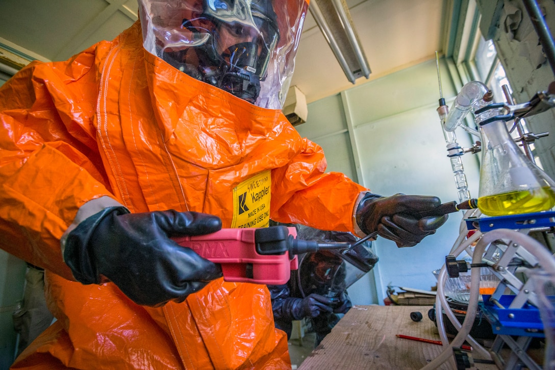 A person wearing a suit holds a device near a beaker of liquid.