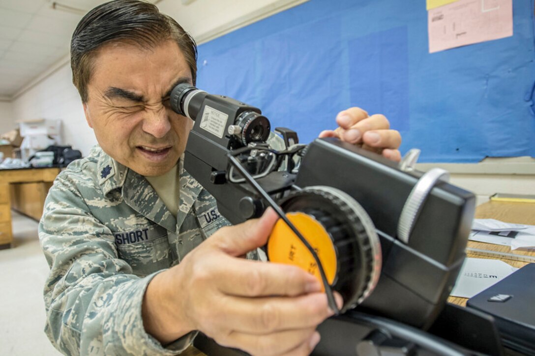 An airman looks through optometry equipment.