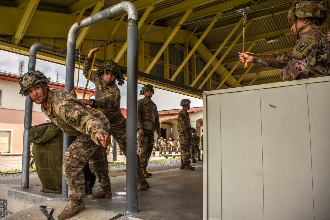 An Army jumpmaster observes soldiers practicing exiting a mock door of an aircraft.