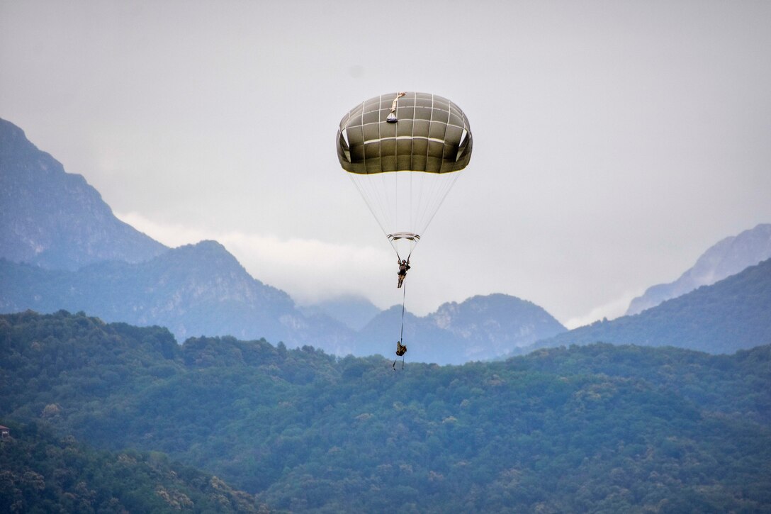 A soldier descends with full chute and prepares to land during airborne operation.