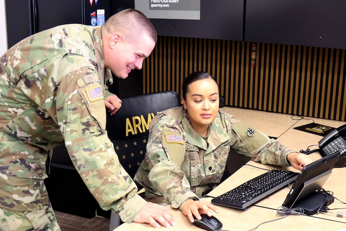 One person sits at a desk while another watches.