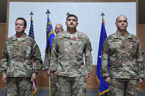 Three Airmen stand on stage at attention
