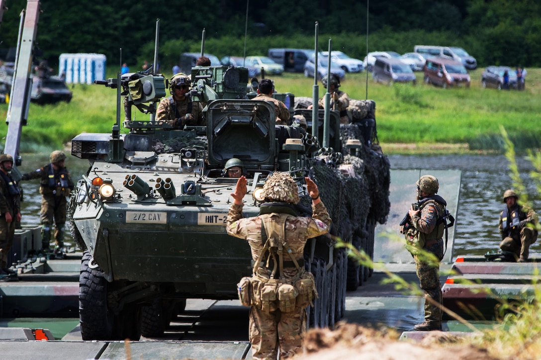 A British soldier guides troops assigned to the 2nd Cavalry Regiment off of an M3 Amphibious Rig Bridge after ferrying them across the Nemen River.