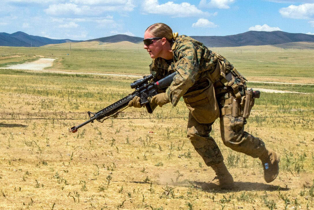 A Marine runs through a field.