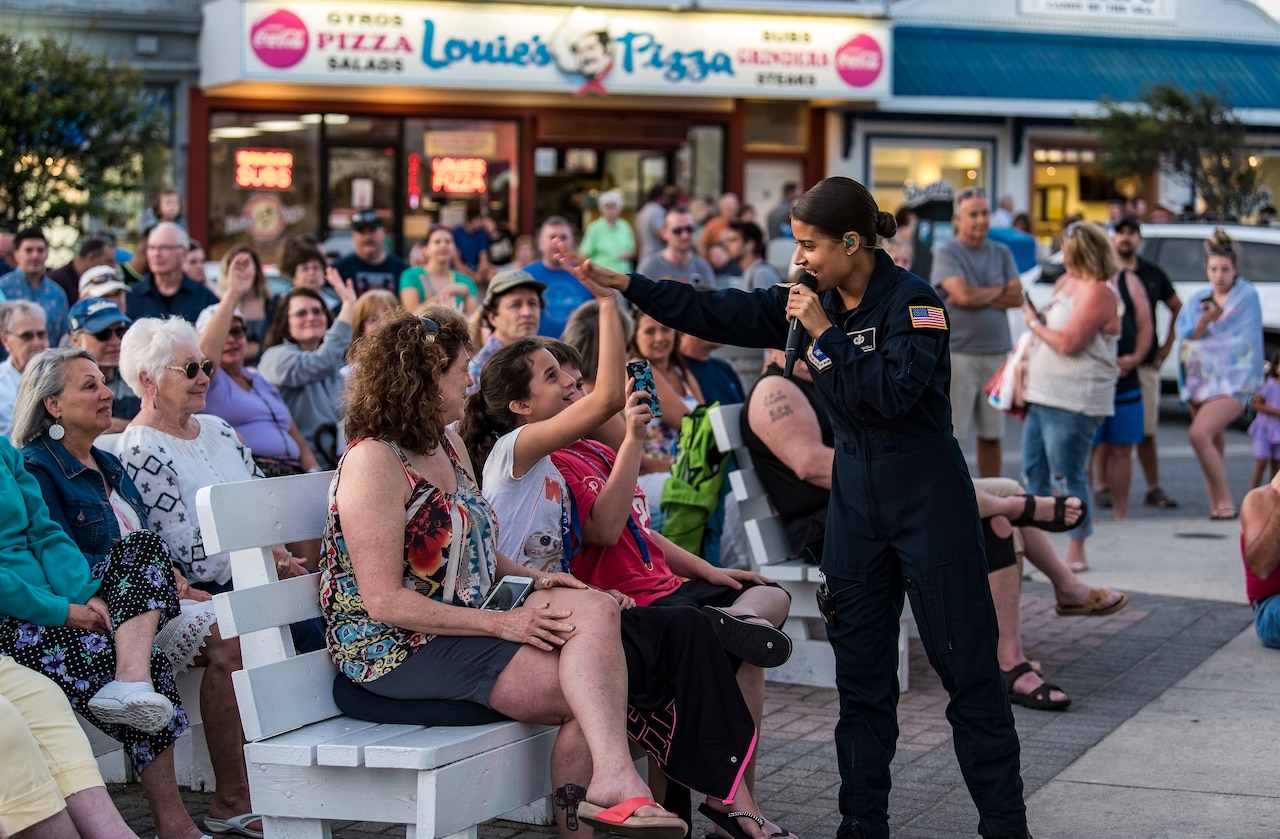 Singer dressed in a blue flight suit and holding a microphone give a high five to a girl seated on a bench.