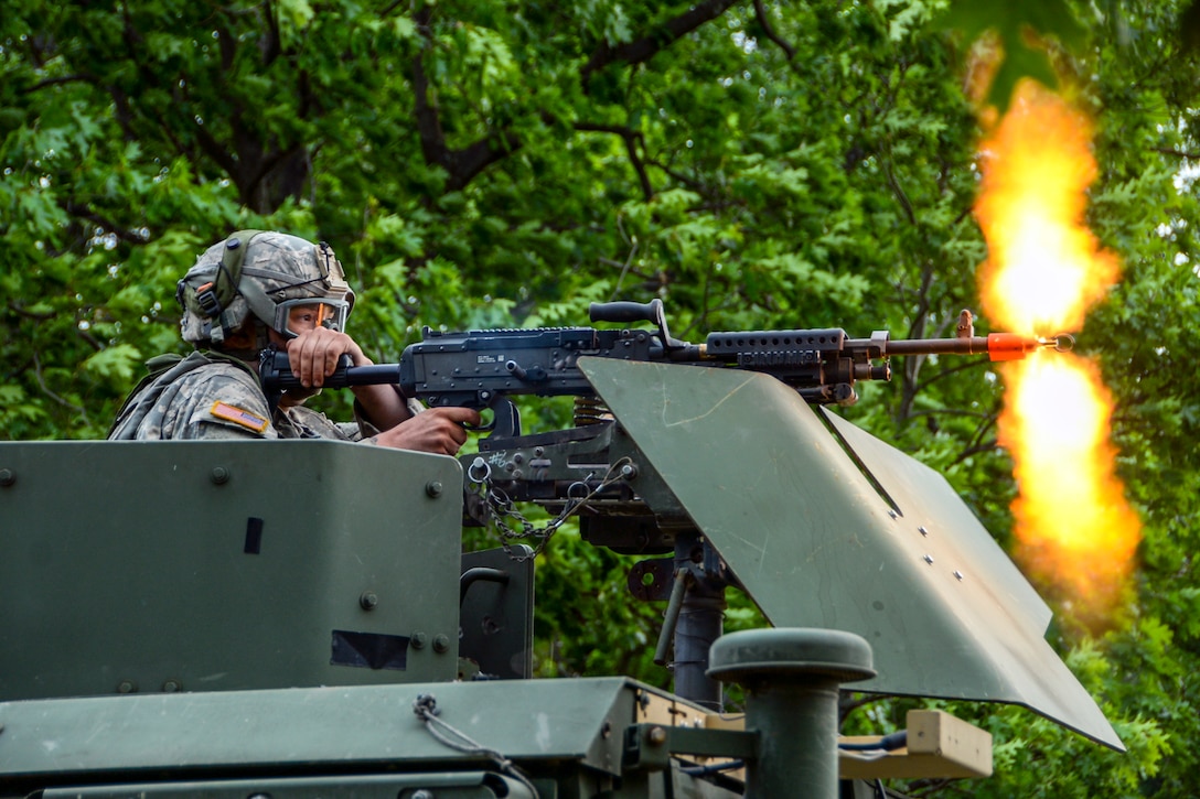 A soldier fires a machine gun from a military vehicle.