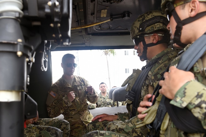 Military personnel talk inside a helicopter.