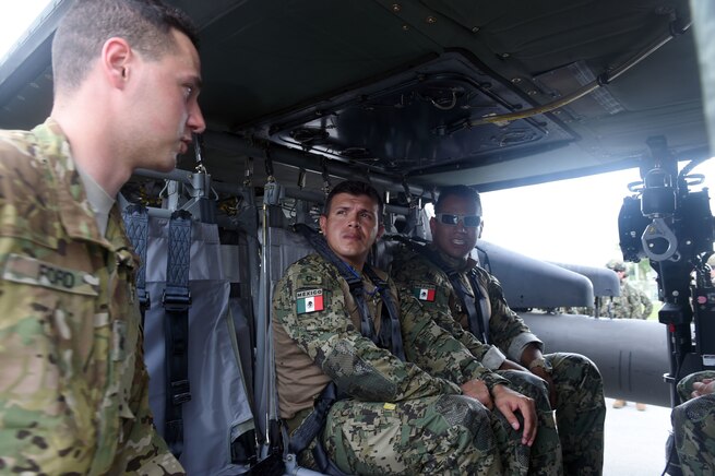 Military personnel talk inside a helicopter.