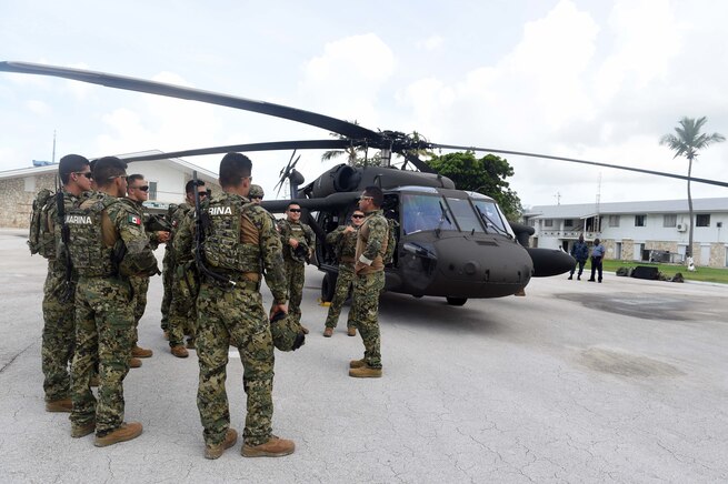 Military personnel talk by a helicopter.