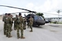 Military personnel talk by a helicopter.